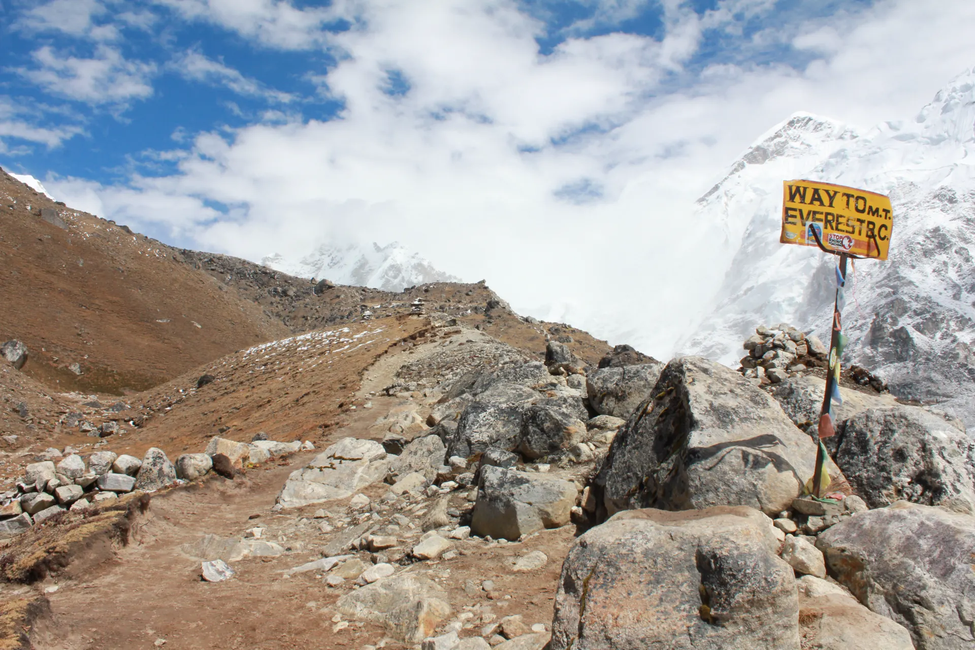 Rocky trail with a signpost above the Khumbu Valley, prayer flags in the distance